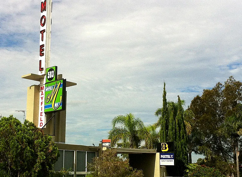 Mayfield Motel’s tall MOTEL pylon sign seen from the footpath on Maitland Road, with the mid-century building behind it.